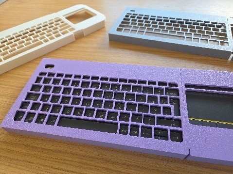 three keyguards in different colours (white, grey and purple) on a wooden surface