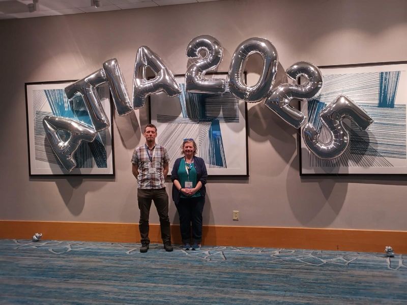 Claire and Fil, the two 2025 AT Scholars standing under a silver ballon arch. The balloons spell out ATIA 2025.