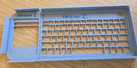 Grey plastic keyguard labelled version 2 on a wooden surface.
