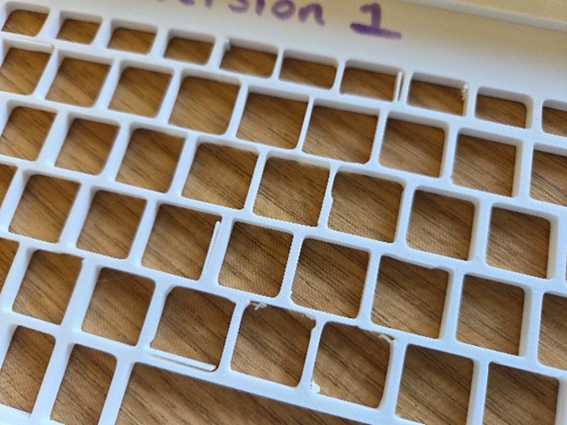 White plastic keyguard labelled version 1 showing rough edges to the key gapson a wooden surface.