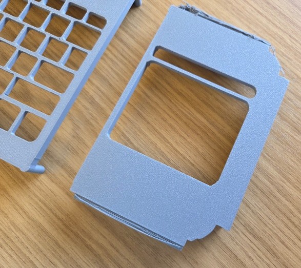 Close up of a grey plastic keyguard showing the sides not fully attached on a wooden surface.